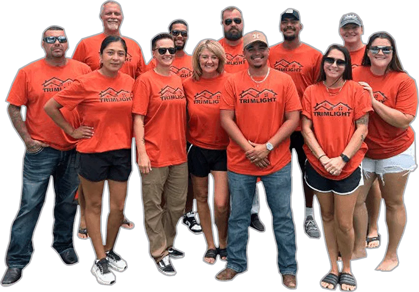 A group of twelve people stand together, smiling, all wearing matching orange Trimlight t-shirts. They are dressed casually, and some wear sunglasses. The background is white and plain.