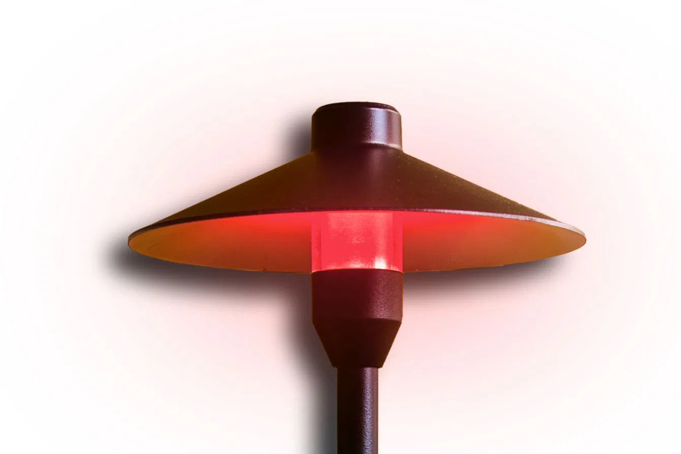 A black outdoor lamp with a wide, conical shade emits a warm red glow from its center, casting a subtle shadow on a white background.