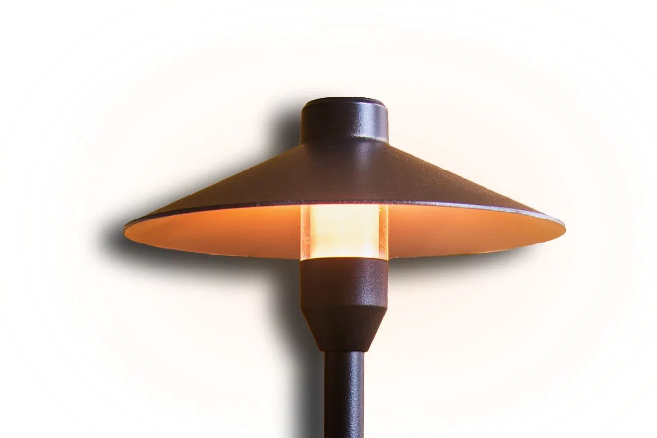 A brown outdoor lamp with a wide, cone-shaped metal shade and a glowing cylindrical bulb, mounted on a black pole, casting a soft shadow on a white background.